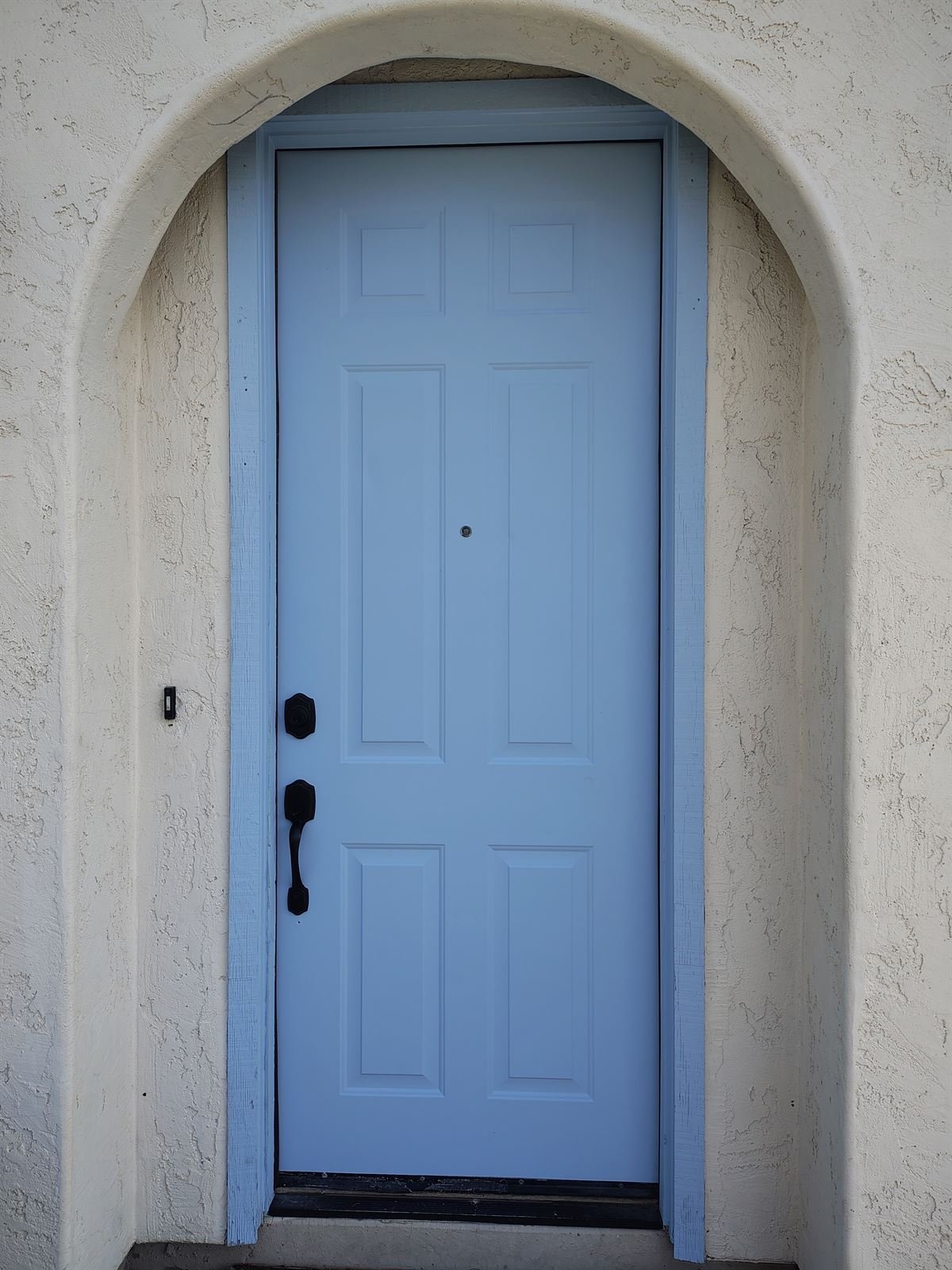 Front door painted soft blue in arched stucco entry